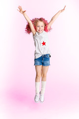 Colored wavy hairs. Little modern hipster girl in fashion clothes, jumping in studio and smiling