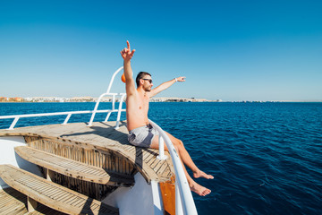 Freedom and travel. Young man sitting on the deck with his back, raising his hands up sea
