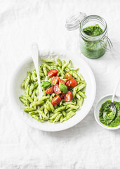 Pasta penne with arugula pesto and cherry tomatoes on light background, top view