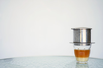 Vietnamese coffee with milk in a glass glass close-up on a transparent glass table. Blurred white and blue background. Side view with copy space