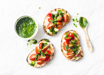 Mozzarella cheese, cherry tomatoes and arugula pesto bruschetta on light background, top view....