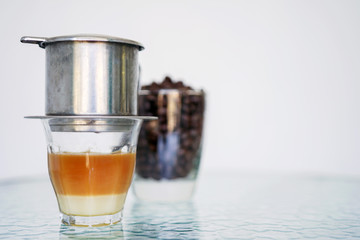 Vietnamese coffee with milk in a glass glass close-up on a transparent glass table. Blurred white and blue background. Side view with copy space