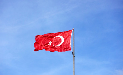 Turkish flag fluttering in the wind in the blue sky. National symbol of the state of Turkey.