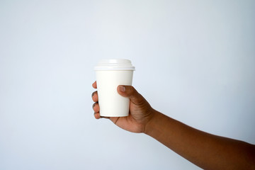 The hand of a dark-skinned man holds a disposable cup for coffee or tea background a white and blue wall. Side view with copy space