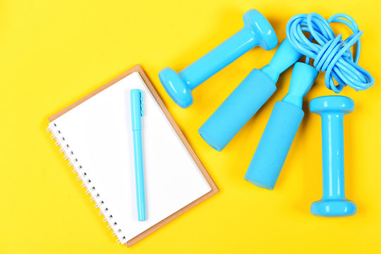 Notebook, pen and gym equipment top view on yellow background