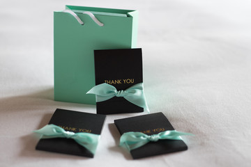 Green bag with black thank you card and green bow on white bed.