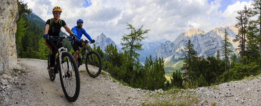Tourist cycling in Cortina d'Ampezzo, stunning rocky mountains on the background. Family riding MTB enduro flow trail. South Tyrol province of Italy, Dolomites.