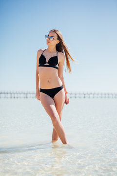 Close-up beautiful luxury slim girl in a black bikini on the beach the ocean. Outdoor summer lifestyle image of young pretty woman outfit and sunglasses, fun ,joy, emotions.