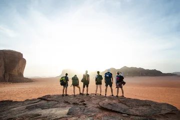 Foto auf Acrylglas Dürre Touristische Freunde auf einer Bergspitze in einer Wüste. Blick auf den Sonnenuntergang. Natur. Touristen genießen einen Moment in der Natur. Wadi Rum Nationalpark - Jordanien
