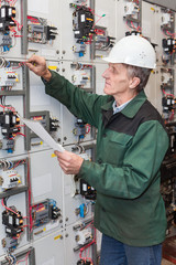 Senior electrician with a screwdriver and wiring diagram in his hand standing near an electric shield