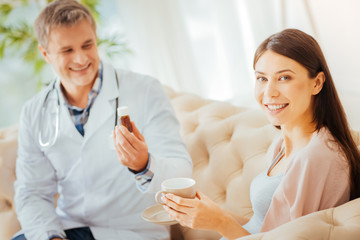 Additional support. Selective focus on a radiant woman smiling into the camera while drinking tea and getting her vitamins during an appointment.