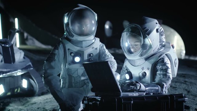 Two Astronauts Wearing Space Suits Work on a Laptop, Exploring Newly Discovered Planet, Send Communicating Signal to Earth. Space Travel, Interstellar Exploration Concept. 