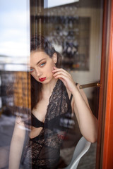 Young sexy woman in black lingerie poses outside the window. Reflection effects