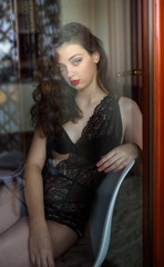 Young sexy woman in black lingerie poses outside the window. Reflection effects