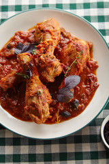 Chicken legs cooked in italian cacciatore style with tomato sauce and fresh basil on green checkered table-cloth