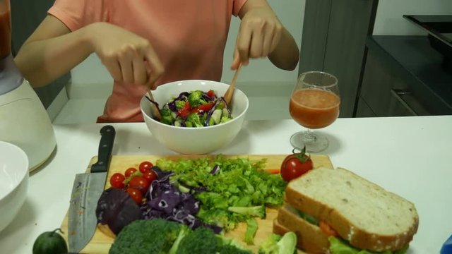 4k of young woman mixing salad while cooking in kitchen