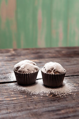 chocolate muffins sprinkled with powdered sugar on a dark wooden table