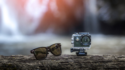 Sunglasses and action cam on top of a brown tree with the waterfall behind.