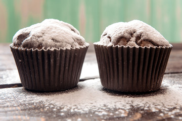 chocolate muffins sprinkled with powdered sugar on a dark wooden table