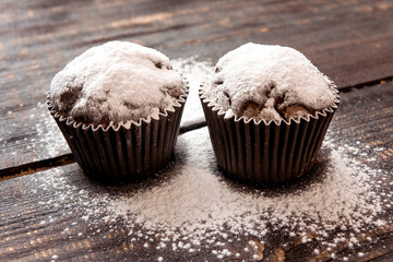 chocolate muffins sprinkled with powdered sugar on a dark wooden table