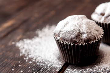 chocolate muffins sprinkled with powdered sugar on a dark wooden table