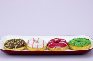 four colored donuts in a tray isolated on lilac background