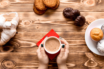 Cup of coffee in female hands on wooden background