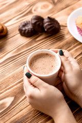 Cup of coffee in female hands on wooden background