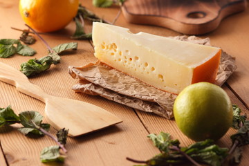 Hard cheese, lemon, lime and mint on a wooden background, wooden spatula, mint leaves with cheese and holes, rustic style, parchment cheese, healthy food, vegan