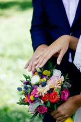 Bride and groom demonstrating rings on their hands against flower bouquet as background.