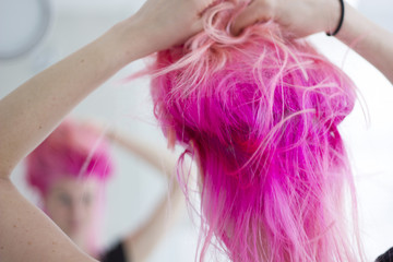 Pink hair woman with a roughed hair looking at the mirror