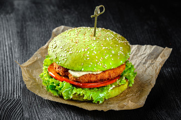 Green Burger fish cutlet and tomato on a black wood background