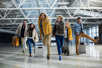 Delighted companions running to airport registration desk. Some of them holding bags in hands