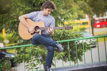 Handsome young man playing guitar outdoors, enjoying his hobby