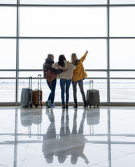 Backs of young companions with suitcases watching aircrafts landing and taking off. One girl is...