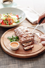 the man in the restaurant with a knife cuts grilled pork ribs. Serving on a wooden Board.