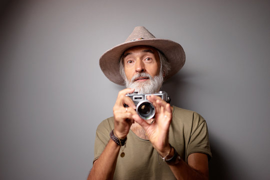 Traveler and photographer. Studio portrait of handsome senior man with gray beard and hat holding photocamera.