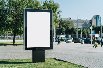 Vertical blank glowing billboard on the city street. In the background buildings and road with...