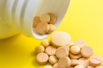 Heap of assorted beige capsules on yellow background.