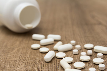 Heap of white capsules on wooden table.