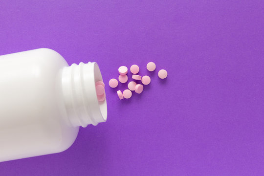 Capsules spilling out of white bottle. Violet background.