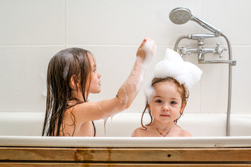 Two little sisters play in a bath.