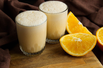 Glasses of milkshake and orange on wooden background over brown cloth