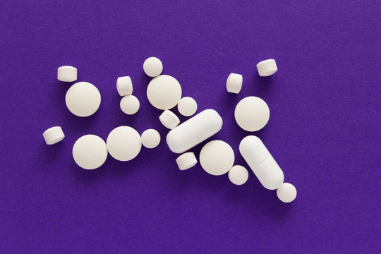 Group of assorted white tablets. Purple background.