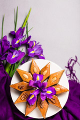 Plate of traditional Azerbaijan baked pastry dessert pakhlava baklava with walnuts for lilac Novruz holiday spring celebration with bouquet of purple flowers fleur de lis on light grey background 