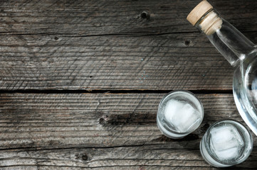 Two shot glasses with cold vodka or gin on wooden table,