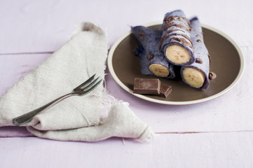 Blueberry pancakes stuffed with whole banana wrapped in a tube and poured with chocolate on wooden...