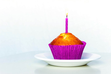 Isolated muffin with purple candle on white background.
