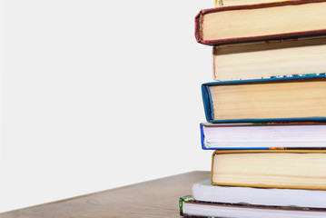 Stack of different books on a table against a white wall background