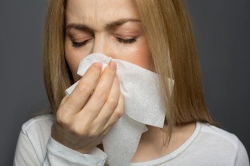 Contagious disease. Cheerless lady covering her nose with tissue and sneezing. Isolated on background